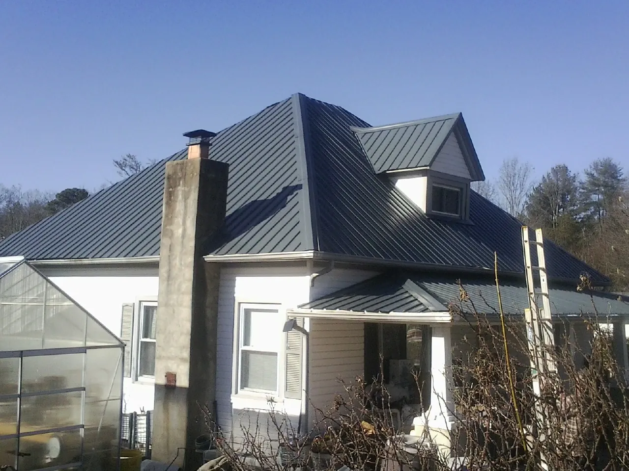 Dark blue standing seam metal roof on a white farmhouse with dormer — Slate & Tile Roof Repair by Roofing Brothers in Massena