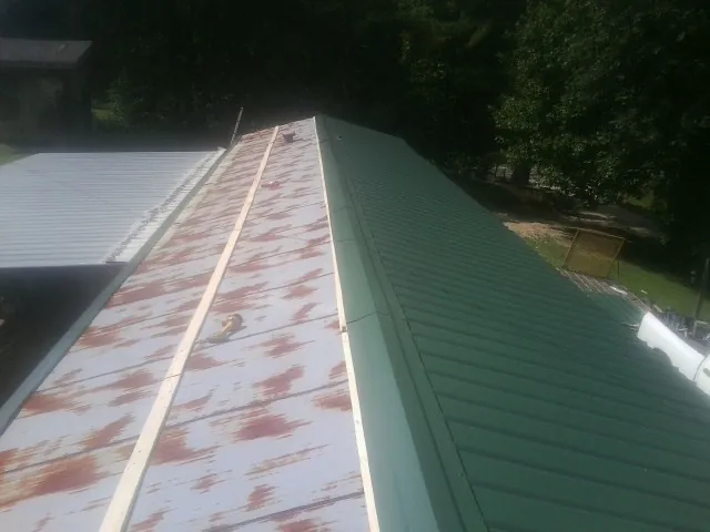 Old rusted panels beside newly installed green metal roofing — Wind Damage Roof Repair by Roofing Brothers in Massena