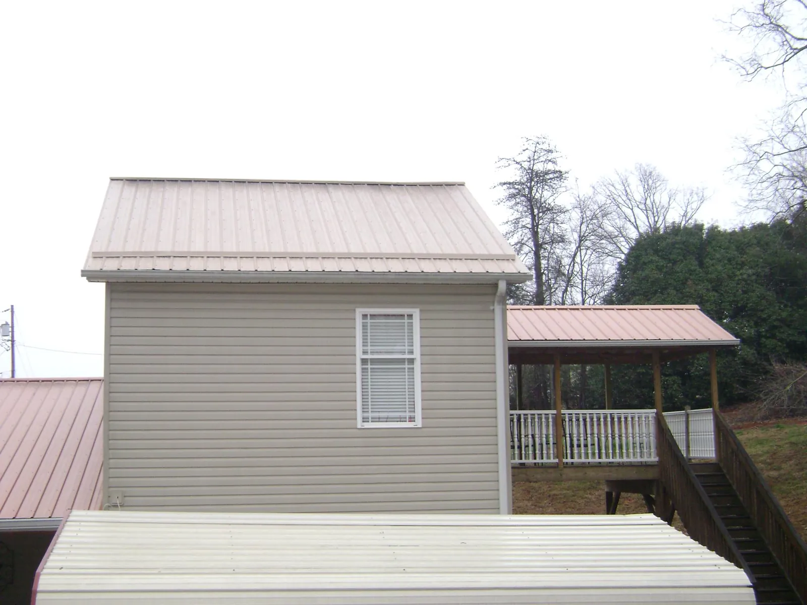 Tan metal roofs on a two story addition and attached porch, from a Roof Replacement job in Massena